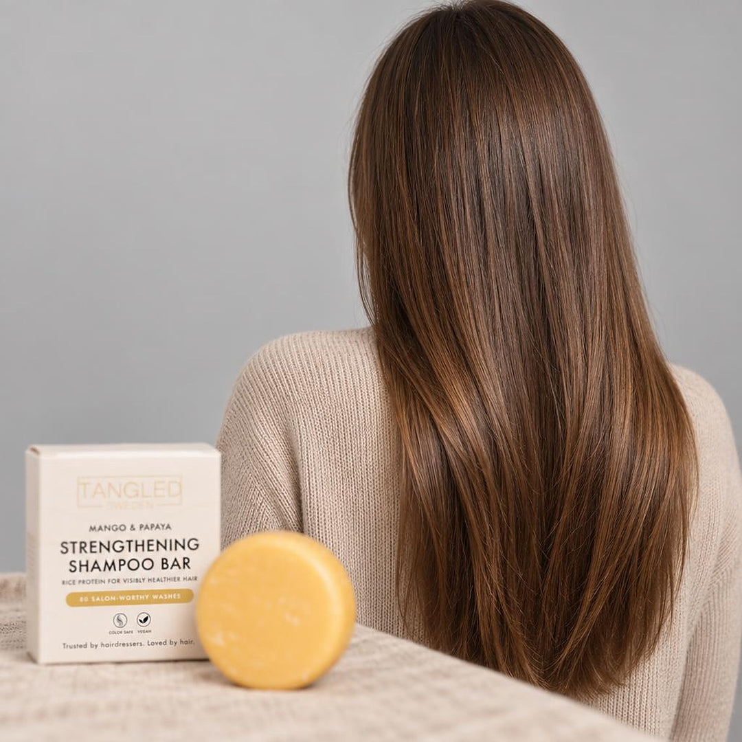 Nainen pitkillä, kiiltävillä ruskeilla hiuksilla takaapäin sekä Tangled shampoopala pakkauksineen